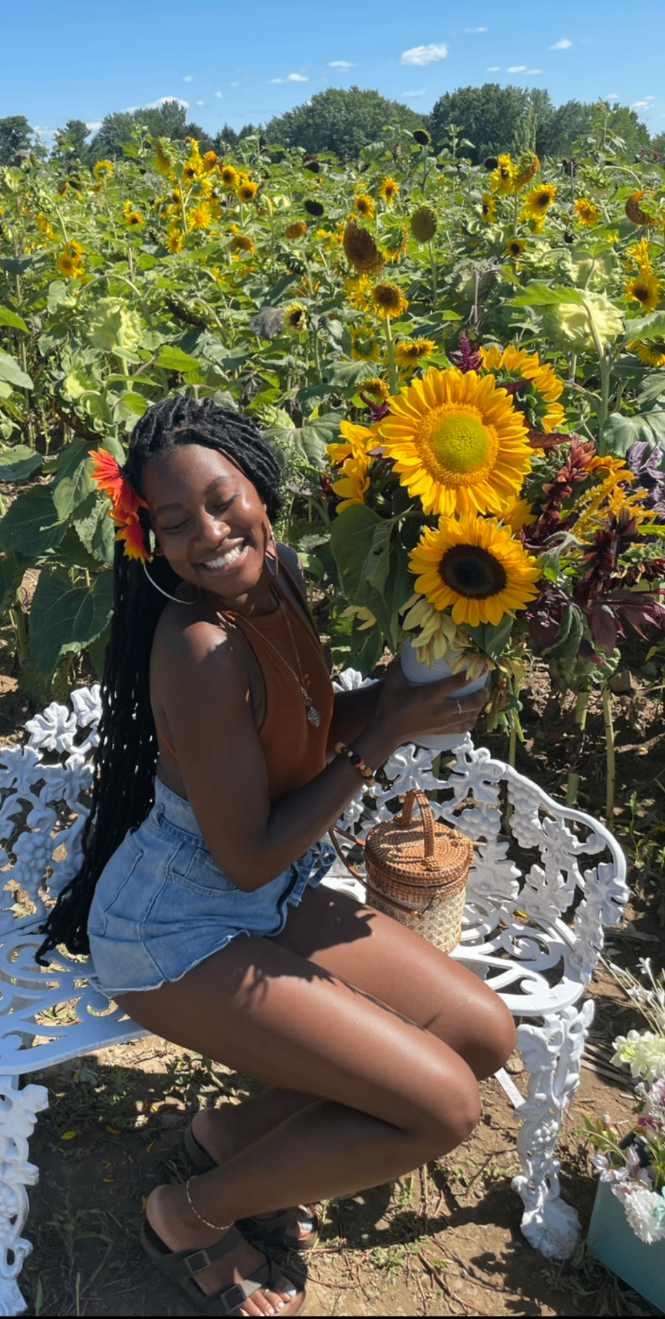Naimah smiling and holding sunflowers in a sunflower field